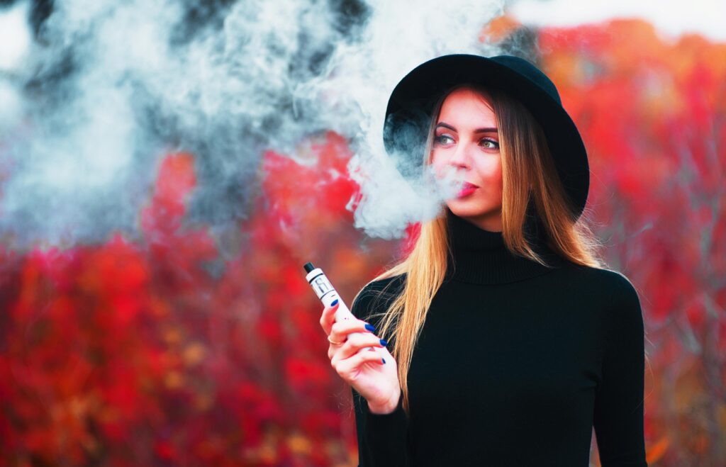 Eine Frau im herbstlichen Look raucht eine E-Zigarette