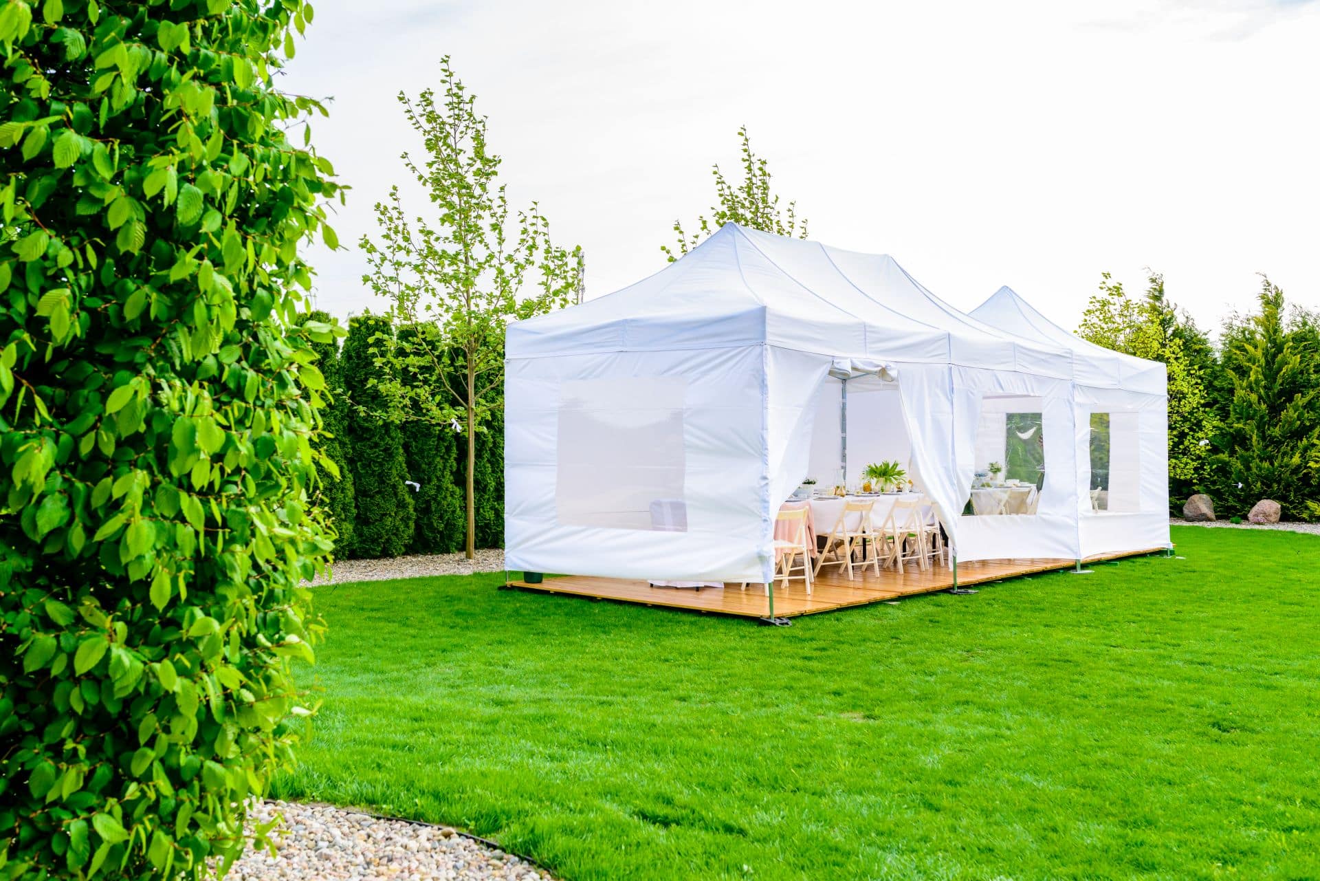 Ein weißes Faltzelt in einem gepflegten Garten, das einen stilvollen und wetterfesten Ort für Feiern bietet, mit der Option eines Pavillons wasserdicht für dauerhaften Schutz.