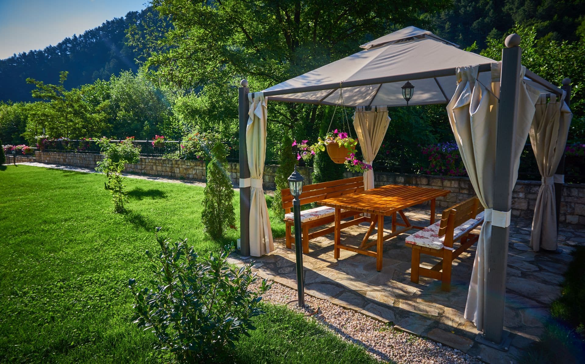 Ein idyllischer Pavillon mit Vorhängen in einem grünen Garten, ideal für gesellige Abende oder ruhige Stunden, wobei die Wahl eines Pavillons wasserdicht zusätzlichen Schutz garantiert.