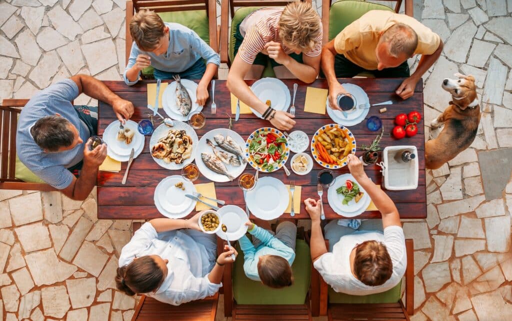 Familie isst gemeinsam gegrillten Fisch und Meze im Garten an einem Holztisch