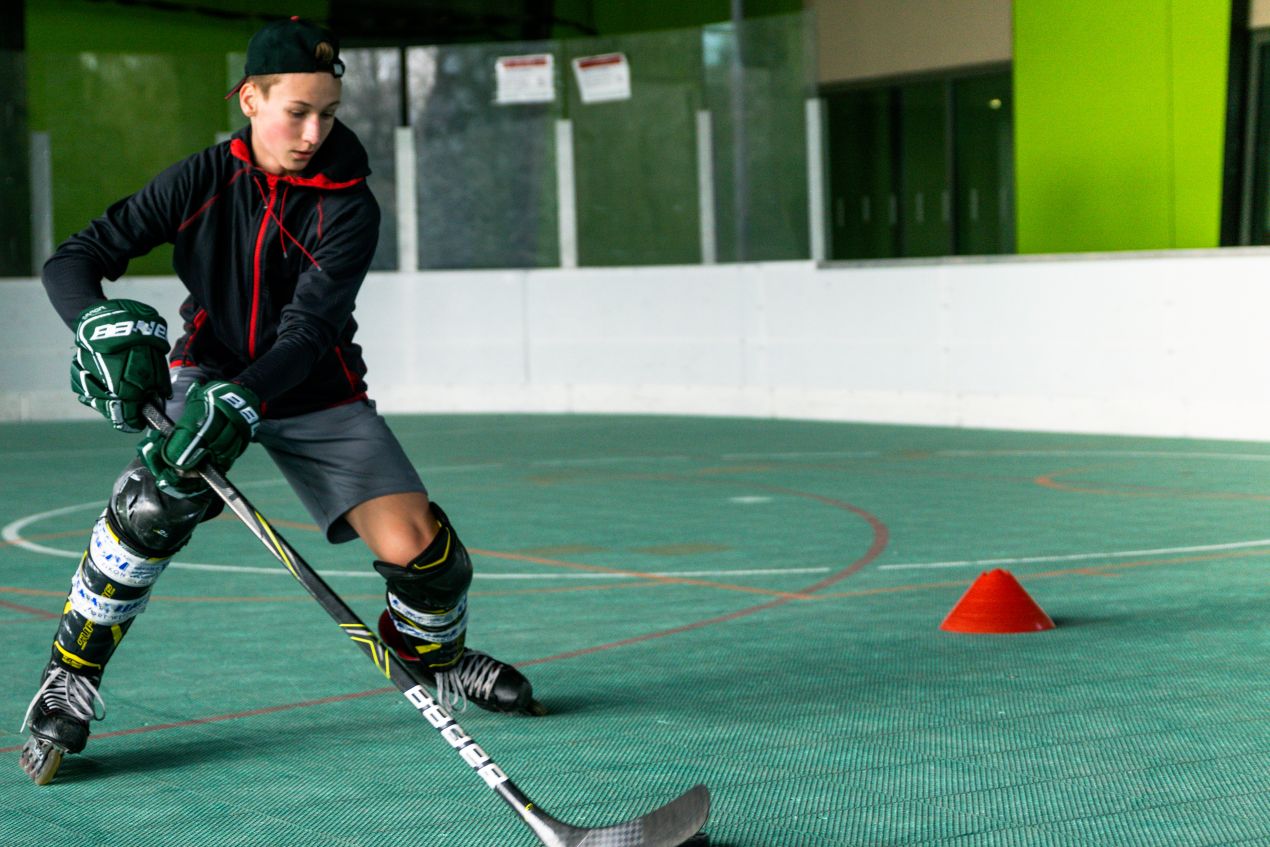 Jugendlicher beim Inlinehockey-Training mit Schlaeger und roten Markierungshuetchen