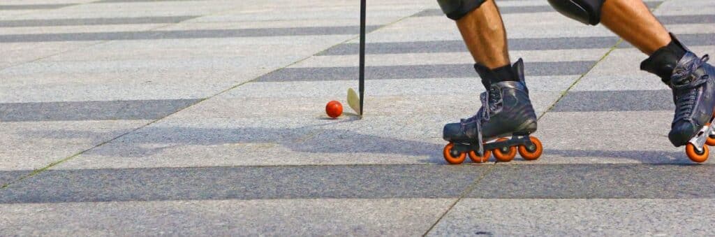 Inlinehockey-Spiel auf Asphalt mit orangem Ball und Schlaeger in der Stadt