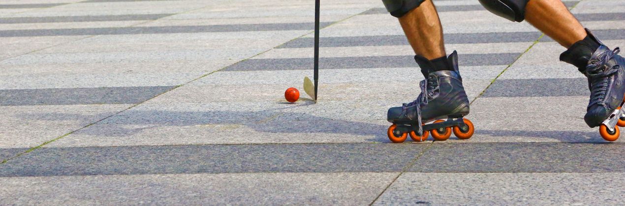 Inlinehockey-Spiel auf Asphalt mit orangem Ball und Schlaeger in der Stadt