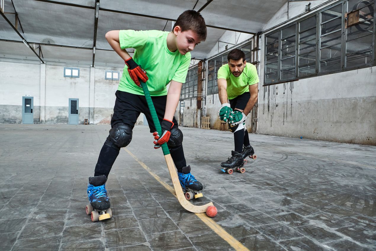 Junge mit Trainer beim Inlinehockey-Training in einer Sporthalle auf Rollschuhen