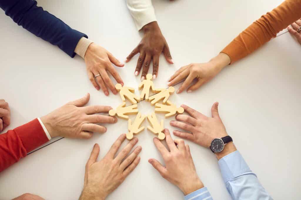Mehrere Haende umkreisen Holzfiguren im Kreis | Betreuungskraft Ausbildung