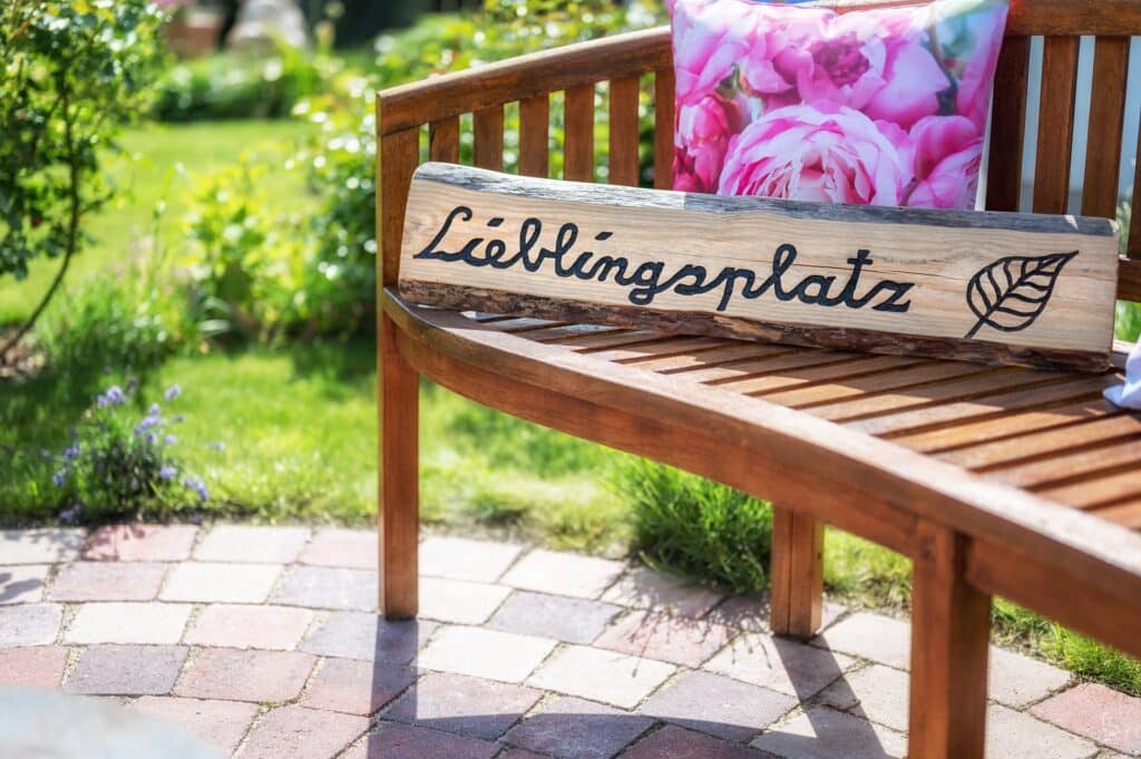 Holzbank mit Lieblingsplatz-Schild in sonnigem Garten | Steingarten